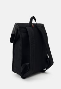 Black fabric backpack with a roll-top design, adjustable shoulder straps, and a small brown leather accent on the top.