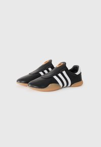 Black athletic shoes with white stripes, soft leather upper, gum rubber sole, and a distinctive circular accent on the tongue.