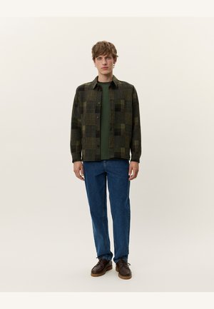 Green and black checkered shirt jacket, button-up, worn over a dark green t-shirt, paired with blue jeans and brown shoes. Simple design, casual fit.