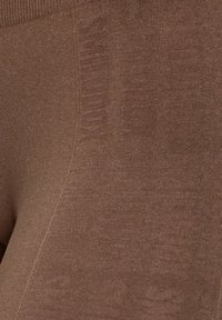 Leggings marroni in tessuto morbido e testurizzato con sottili motivi sui lati e una fascia elastica liscia in vita.