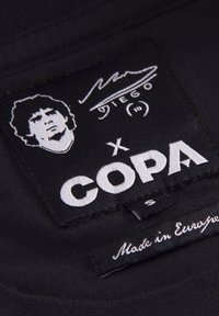 Sort stoftags med hvid tekst og en broderet grafik af et ansigt. Teksten læser "DIEGO" og "COPA," med "Made in Europe" nedenfor.