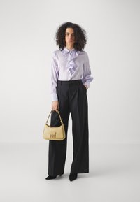 Light purple, ruffled blouse with button-down collar paired with high-waisted, black wide-leg trousers. Holding a textured, light yellow handbag.