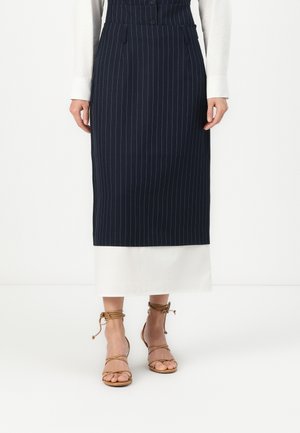 Gonna a righe blu navy con orlo bianco, caratterizzata da vita alta e tasche frontali, abbinata a sandali beige con cinturini. Tessuto dalla consistenza morbida.