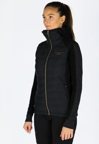 Gilet imbottito nero con colletto alto, zip dorata e logo ricamato. Caratterizzato da un design aderente, maniche lunghe nere a contrasto e una superficie liscia.