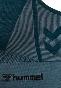 Sportbeha in teal en donkerblauwe tinten, met ribbelstructuur, chevronpatronen en logootje onderaan.