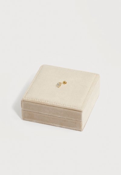 Μονόχρυσο σκουλαρίκι με καθαρό, σταγόνα σε σχήμα κοσμήματος, τοποθετημένο πάνω σε βελούδινο μπεζ κουτί για κοσμήματα.