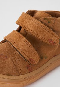 Braune Wildleder-Stiefeletten mit doppelten Klettverschlüssen, strukturierten Oberflächen und einer Gummisohle mit dezenten bunten Mustern.