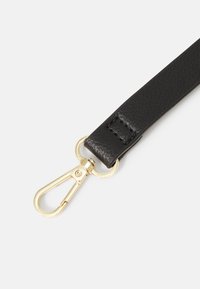 Sangle en cuir noir texturé avec un fermoir pivotant en métal doré attaché à un anneau rond doré sur fond blanc.