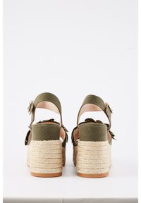 Sandales compensées vert olive avec brides autour de la cheville et talons en corde tissée, vues de dos sur fond blanc.
