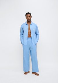 Σετ πιτζάμες με γαλάζιες ρίγες που περιλαμβάνει πουκάμισο με κουμπιά και φαρδιά παντελόνια, κατασκευασμένο από απαλό ύφασμα με διακριτικές κεντητές λεπτομέρειες.