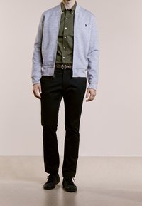 Jasnoszara bomberka na zamek nawiązana do oliwkowozielonej koszuli, czarnych spodni i czarnych sneakersów. Kurtka ma ściągacze przy rękawach i logo.