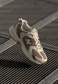 Lightweight running shoe in beige and brown with mesh and synthetic overlays. Features a padded collar and rubber outsole with textured grip.