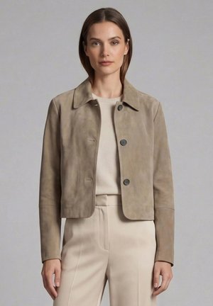 Femme portant une veste boutonnée en daim beige clair par-dessus un pull crème avec un pantalon taille haute assorti sur un fond gris uni.