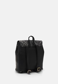 Schwarzer Rucksack mit einer texturierten Schlangenhautklappe, zwei verstellbaren Schulterriemen und Akzenten aus goldfarbenem Metall. Glatte Oberfläche und strukturiertes Design.