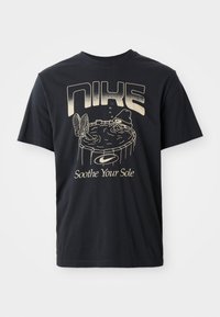 Sort bomulds t-shirt med et grafisk print af en figur i et boblebad, med "NIKE" og "Soothe Your Sole" i lys gyldent skrift.