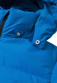 Giacca isolante blu con cappuccio, tessuto liscio, bottoni a pressione e zip nera. Dettagli di cucitura visibili sul corpo.