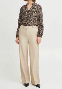 Blusa con stampa leopardata e scollatura a V, maniche lunghe, abbinata a pantaloni beige a vita alta. Vestibilità slim, tessuto leggero e design strutturato.
