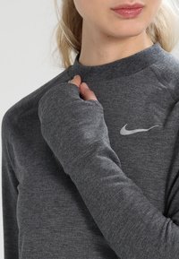 Grijze lange mouwen shirt met een hoge hals. Kenmerkt zich door een slim fit ontwerp, zachte stof en een klein wit Nike-logo op de borst.