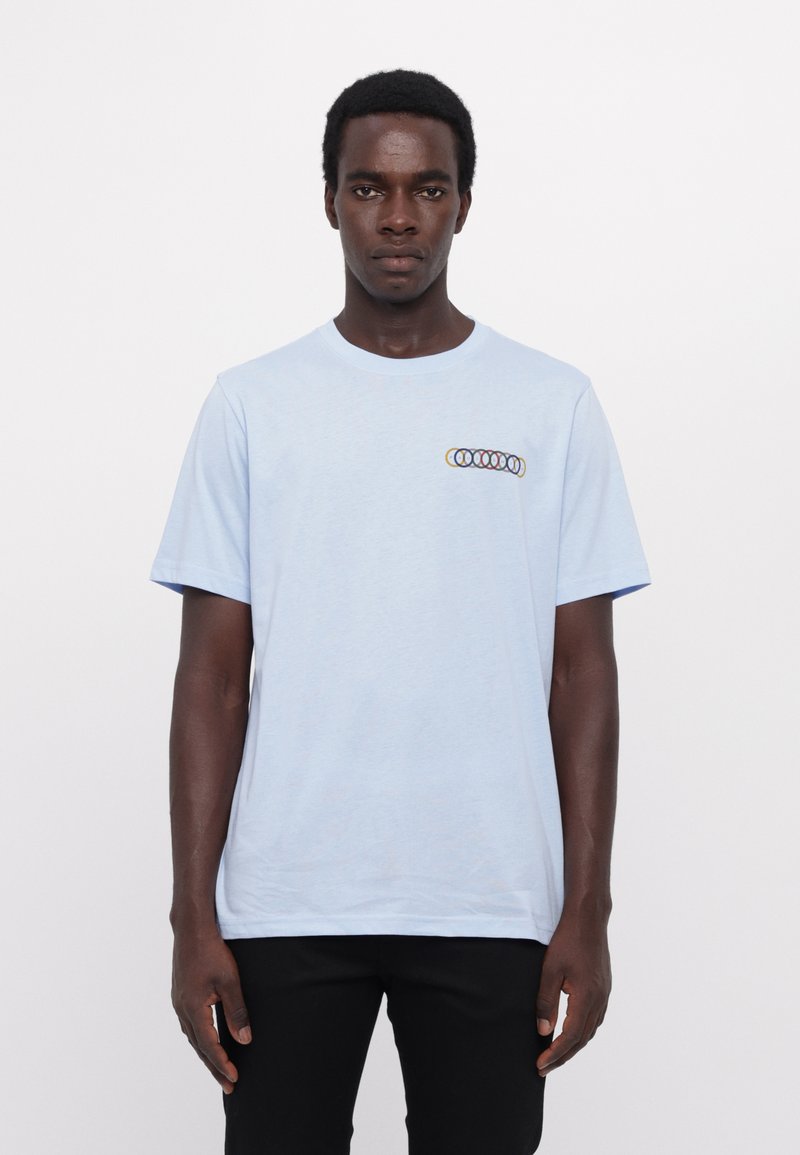 Lyseblå bomulds T-shirt med korte ærmer, prydet med et flerfarvet cirkulært grafisk design på brystet. Glat tekstur, almindelig pasform.