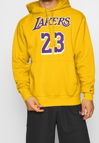Sweat à capuche jaune avec "LAKERS" et le numéro "23" en violet sur le devant, poche kangourou et capuche à cordon. Logo Nike sur la manche.