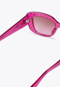 Occhiali da sole trasparenti rosa con motivo a pois, montatura angolare, lenti sfumate e dettagli lucidi sulle tempie.
