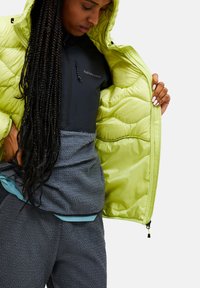 Peak Performance pufferjakke i lys limegrøn med quiltet tekstur, lynlås foran og lagdelt mørk fleece inderside.