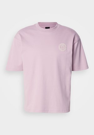 Világos rózsaszín pamut póló kerek nyakkivágással, rövid ujjakkal és egy kis, texturált logóval az bal mellrészen. Simább tapintású anyag.