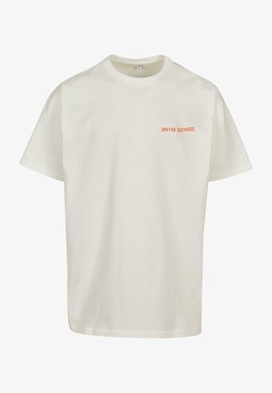 T-shirt en coton crème à manches courtes avec le texte "9N1M SENSE." en orange, situé sur la zone de la poitrine gauche. Encolure ras du cou classique.