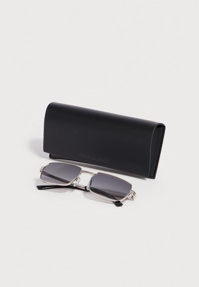 Lunettes de soleil rectangulaires à monture argentée avec verres foncés à côté d'un étui de protection noir DSQUARED2 sur fond blanc.