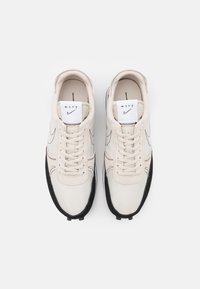 Beige hardloopschoenen met een bovenwerk van mesh, zwarte suède accenten en witte veters. Kenmerkt een geborduurd logolabel op de tong en een gestructureerde buitenzool.