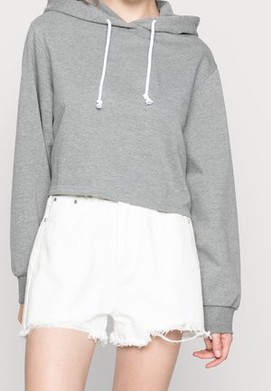 Person trägt einen grauen cropped Hoodie mit weißen Kordeln und hoch taillierte weiße Denim-Shorts mit ausgefransten Säumen.