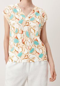Blouse à manches courtes en tissu léger avec un motif floral abstrait coloré en turquoise, rose et or sur fond crème. Col en V.