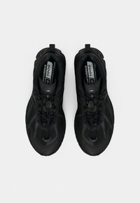 Baskets de sport noires avec un dessus en tissu texturé, affichant un design épuré, des lacets élastiques et un col rembourré pour le confort.