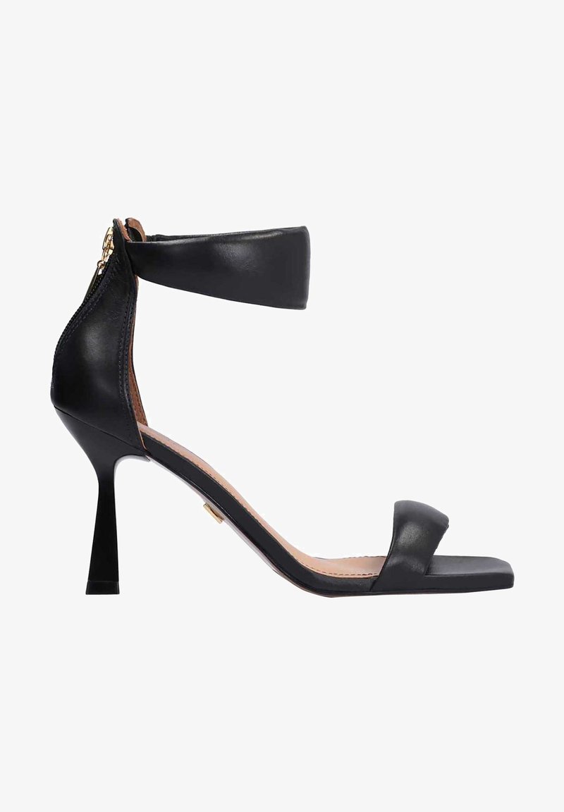 Sandale à talon haut en cuir noir avec bride cheville, fermeture éclair arrière et bout ouvert sur fond blanc.