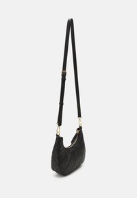 Black quilted handbag with a curved shape, featuring a zip closure and a long adjustable strap. Gold hardware accents add detail.