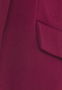 Burgundy fabric with a smooth texture, featuring a pocket detail on the right side, cut in a tailored style.