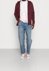 Vinröd zip-up hoodie över en rosa tie-dye T-shirt, kombinerad med ljusblå raka jeans och rosa kanvas sneakers.