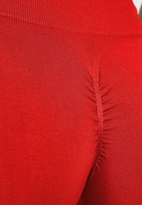 Rote Leggings mit gerippter Textur und gerafftem Nahtdetail auf der Rückseite. Figurbetontes Design ideal für Sportbekleidung.