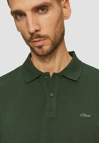 Dunkelgrünes Poloshirt aus strukturiertem Stoff, mit einer Zweiknopf-Leiste und gesticktem "s.Oliver"-Logo auf der Brust.