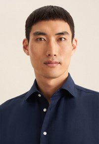 Donkerblauw overhemd met knopen en kraag, van textuurstof, met lichtgekleurde knopen. Heeft een getailleerde pasvorm en een gladde afwerking.