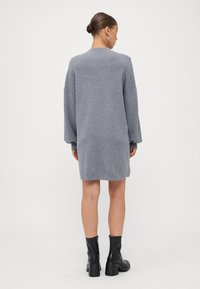 Gray knitted dress with long sleeves and a relaxed fit, reaching mid-thigh. Worn with black ankle boots featuring a chunky heel.