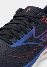 Svart løpesko med teksturert mesh-overdel, grå snørebånd, blå og røde detaljer, og en hvit mellomsole med en svakt gradient effekt.