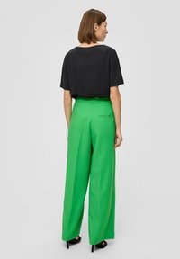 Zwarte korte mouwen top gecombineerd met groene wijde broekspijpen. Soepele stof, effen kleuren, minimalistisch ontwerp, met een achterzakdetail op de broek.