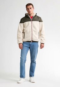 Beige Fleecejacke mit einem olivgrünen Einsatz, Reißverschluss vorne und Kapuze. Verfügt über zwei Seitentaschen und ein kontrastierendes rotes Reißverschlussdetail.