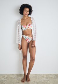 Conjunto de bikini floral con un top sin tirantes y braguitas de cintura alta a juego, complementado con un cover-up de encaje blanco. Textura suave, colores vibrantes.