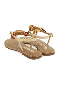 Sandales plates beiges avec une semelle intérieure douce semblable à du daim. Dotées d'accents de chaîne multicolores sur les brides, maintenues par une boucle.
