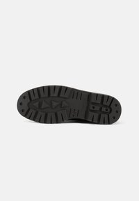 Suela de zapato de goma negra con un diseño de textura. Presenta patrones triangulares y rectangulares para agarre, con surcos y canalizaciones claramente definidos.