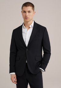 Tume meriinovillane bleiser, mis on valmistatud siledast kangast, ühe nööbi kinnitusega, erinevate lapeltega ja kahe esise taskuga. Kantud valge särke üle.