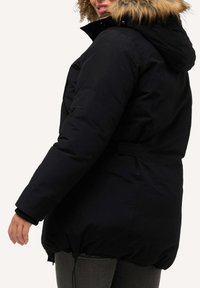 Svart pufferjacka med en huva som är fodrad med päls, midjan är åtstramad och nederkant är elastisk. Har vattentätt material och ribbade manschetter för värme.