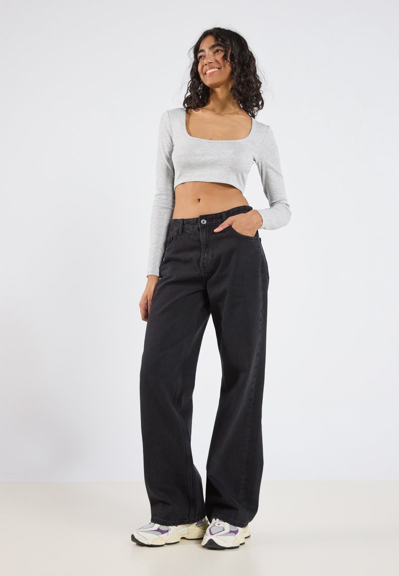Szürke, hosszú ujjú cropped top négyzet alakú kivágással, amelyet magas derekú fekete, széles szárú farmerral és lila részletekkel ellátott fehér sportcipővel párosítanak.
